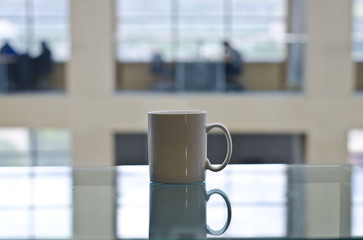 A solo blank white mug on the glass table in the study of the local library. 