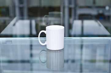 A blank white coffee mug on a glass table in the study of the library. 