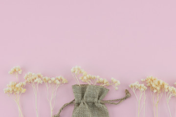 Sackcloth bag with white dried flowers on pastel pink background with copy space 