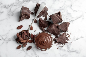 Bowl with tasty melted chocolate, chunks and cocoa beans on table, top view