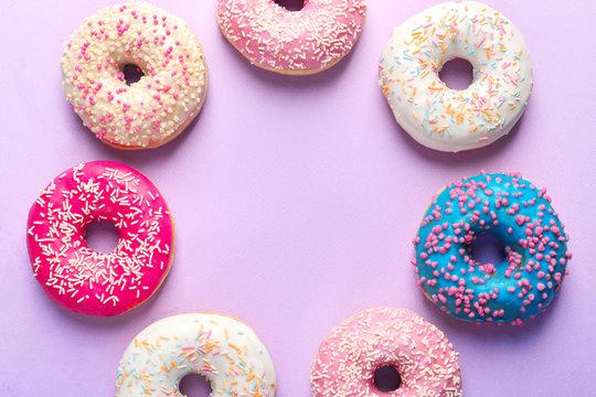 Frame made of delicious doughnuts on color background, top view