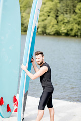 Portrait of a handsome man in black diving suit standing with paddleboard on the beach