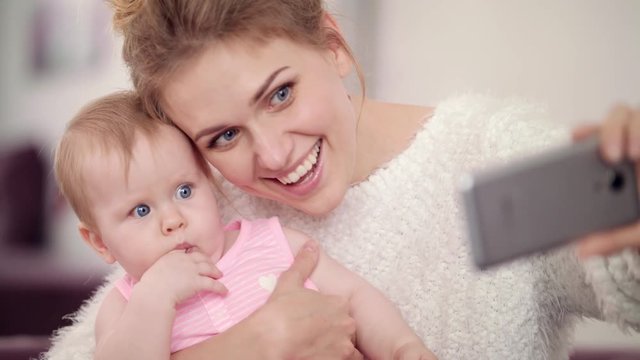 Smiling mother making selfie photo with baby girl. Close up of mom with child taking mobile selfie. Woman with kid mobile photo. Phone selfie of happy mother with infant