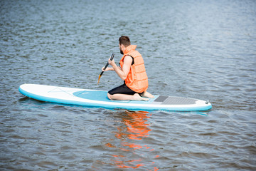 Man in life vest learning to swim with oar on the standup paddleboard on the lake