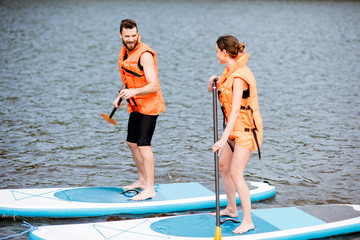 Couple in life vests learning to row on the stand up paddleboard on the lake