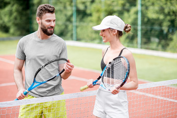 Young couple having fun standing together on the tennis court relaxing after the match outdoors