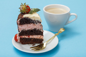 Piece of homemade chocolate cake decorated with fresh strawberries and leaves of mint on white plate with fork and cup of coffee