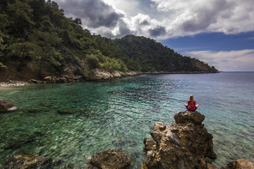 girl sitting on a cliff in mountains near mediterranean sea