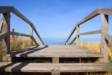 wooden bridge leads across the dunes on the beach of the baltic sea to the water, clear blue sky with copy space