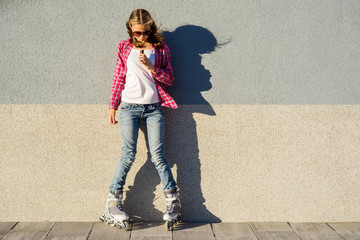 Beauty teen model girl has a chocolate bar, shod in rollers, takes chocolate, on gray wall...