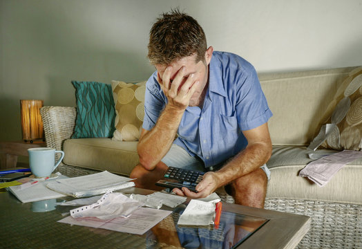 young attractive worried and stressed man at home calculating month tax expenses with calculator accounting payments doing bank paperwork in stress