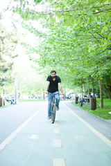 Young bearded man riding a bicycle in the park in summer