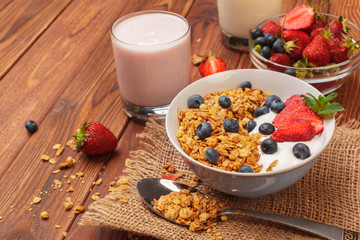 Bowl of homemade granola with yogurt and fresh berries on wooden background