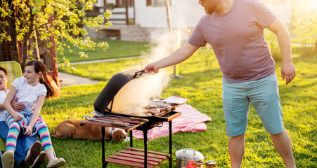 Man is opening grill cap releasing all the steam and arom of meat being grilled inside of it on a...