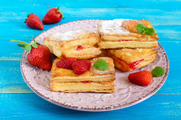 Sweet tasty puff pastry dessert on plate on wooden background. Delicious homemade cookies with strawberry jam, berries and sugar powder.