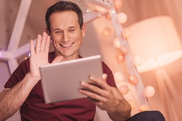 Internet communication. Joyful nice positive man smiling and waving his hand while making a video call