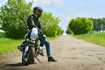 Stylish biker and his beautiful motorbike stoped on a abandoned road. Motorcycle background.