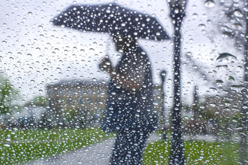 rain drops on glass with blurred background from man holding blue umbrella ,vintage