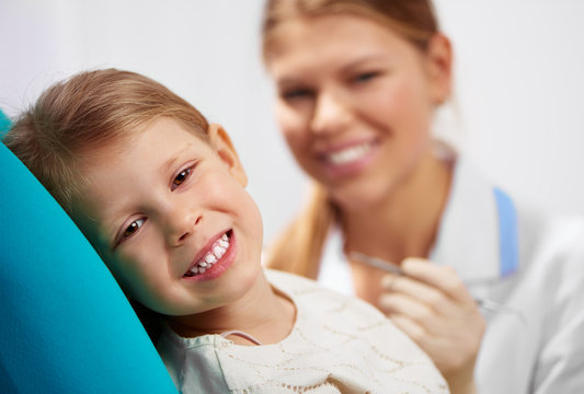 Smiling girl sitting at dentist chair, examining teeth. Dental care concept.  