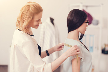 Delicate figure. Close up of young skilled designer taking measurements of beautiful girl while standing behind her back