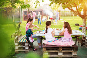 Adorable children are having a picnic meal at the table under the tree while thier parents are grilling in backyard. © Dusan Petkovic