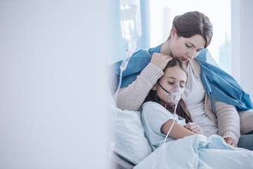 Worried mother taking care of daughter with oxygen mask in the hospital