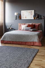 Grey rug in front of a king size bed with pillows and a painting above in a simple bedroom interior