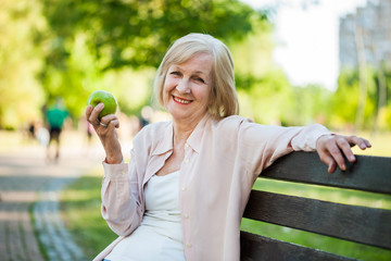 Adult woman sitting in park and eating apple.