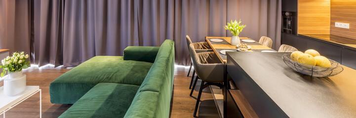 Header of living room interior with sofa and kitchen area with a dining table, chairs, kitchen island and bowl of oranges