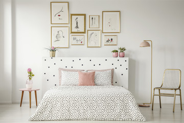 Bright bedroom interior with dotted sheets and headrest, double bed, gold accents and art gallery...