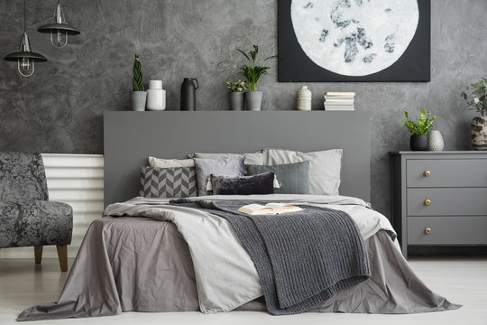 Moon poster on concrete wall above bed with bedhead in grey bedroom interior. Real photo