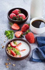 Organic Healthy Breakfast Food. Cup of black coffee and Granola with greek yogurt and strawberry on gray concrete table background.