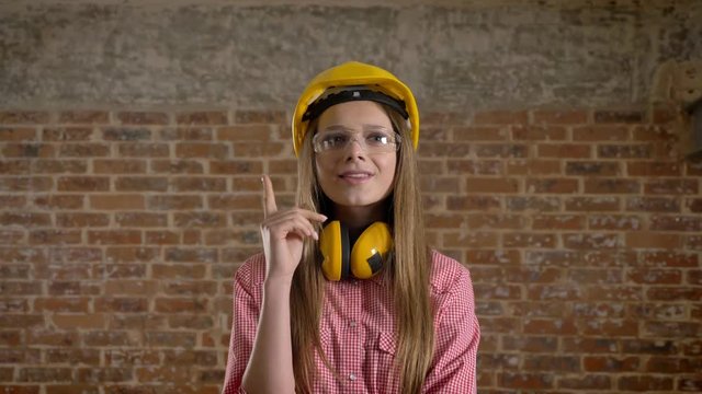 Young butiful girl builder gets idea, thinking process, brick background.