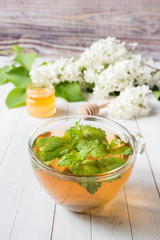 Cup of tea with mint on a wooden table with white lilac flowers