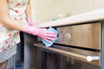 Woman's hand with pink protective gloves cleaning oven door. People, housework, cleaning concept