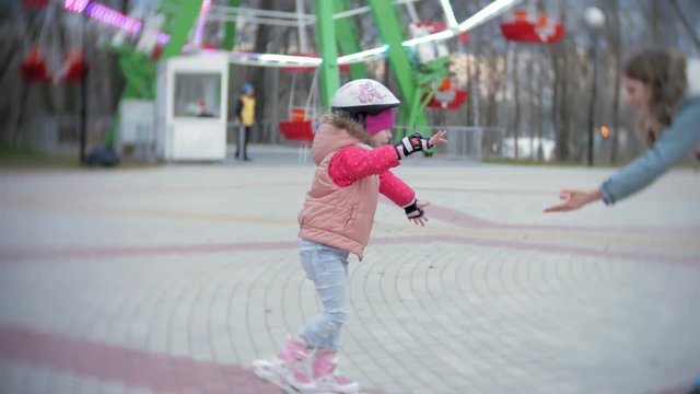 Mom and daughter ride on roller skates. Girl learning to roller skate, and falls. Mom teaches daughter to ride on rollers