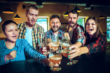 Sport, people, leisure, friendship and entertainment concept - happy football fans or male friends drinking beer and celebrating victory at bar or pub