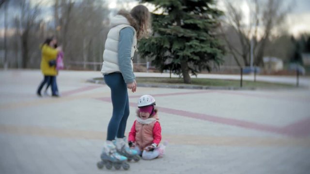 Mom and daughter ride on roller skates. Girl learning to roller skate, and falls. Mom teaches daughter to ride on rollers