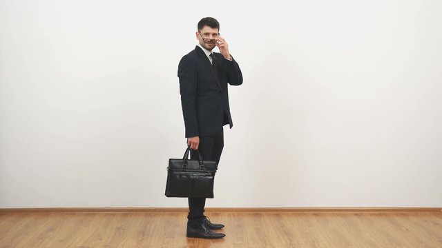 The businessman in glasses walking with a bag on the white wall background