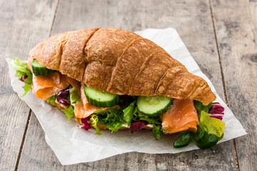 Croissant sandwich with salmon and vegetables on wooden table.