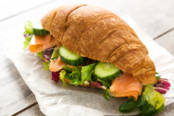 Croissant sandwich with salmon and vegetables on wooden table.