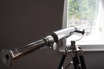 Beautiful old metallic telescope on a tripod watching out of the window