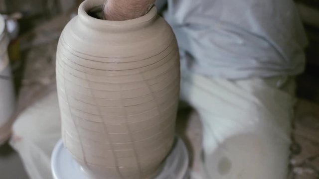 Closeup potter stretches jar by hand on potter's wheel