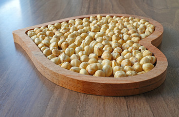 Hazelnut in heart-shaped wooden bowl on wooden table
