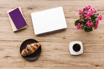 flat lay with laptop, books, cup of coffee, croissant on plate and kalanchoe plant on wooden tabletop