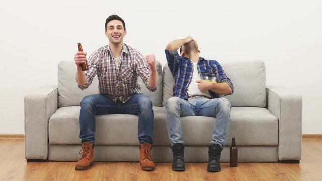 The two men watching a football on the sofa on the white wall background
