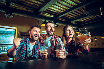 Sport, people, leisure, friendship and entertainment concept - happy football fans or male friends drinking beer and celebrating victory at bar or pub
