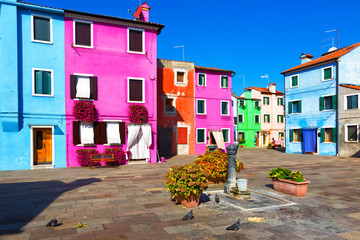 Fototapeta na wymiar A small courtyard in Burano, with colored walls of houses, a column for water and flowers, Italy