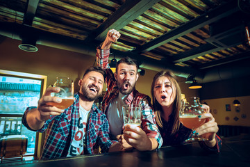 Sport, people, leisure, friendship and entertainment concept - happy football fans or male friends drinking beer and celebrating victory at bar or pub