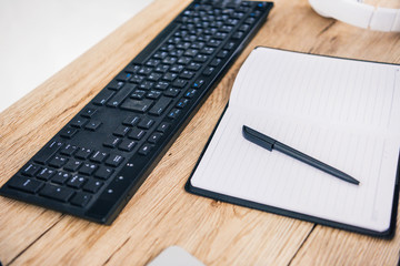 closeup shot of computer keyboard, empty textbook with pen and headphones at table